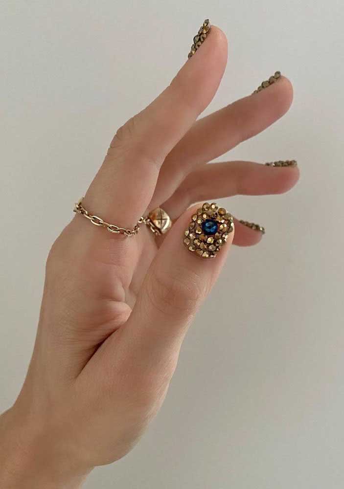 Mas se você quer apostar em um visual com muito estilo e atitude, confira estas unhas decoradas com pedras douradas com um ponto central azul.