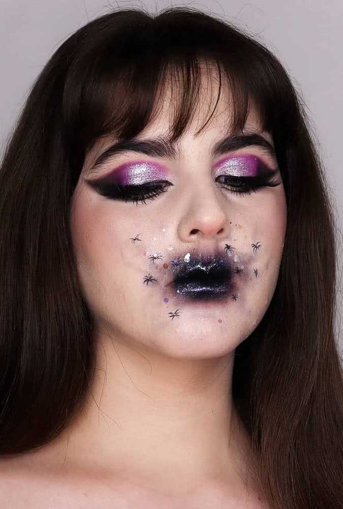 O pincel do delineador também é perfeito para fazer as aranhinhas que rodeiam os lábios esfumados de preto com bastante glitter desta maquiagem de halloween glam.