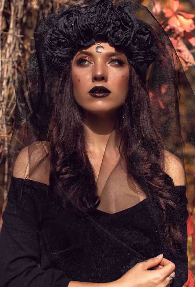 Maquiagem de halloween bruxa num visual all black com sardas em formato de estrela na maçã do rosto, lua crescente na testa e batom.