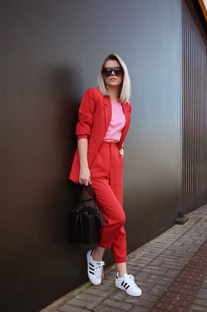 Para enfrentar o dia de trabalho com muito estilo e conforto, um conjunto de alfaiataria vermelha, blusa rosa e tênis casual branco. 