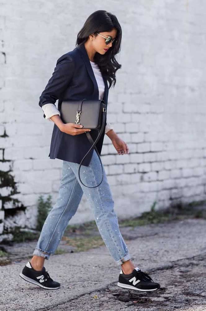 Outra ideia de look com tênis para o trabalho, dessa vez com um modelo casual preto combinando com calça jeans clara, blusa branca e um blazer azul marinho.