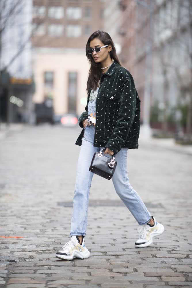 Visual num estilo urbano com calça jeans clara, sneakers chunky banco, camiseta e jaqueta verde escura.