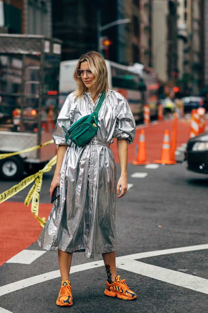 Look com tênis para fashionistas que querem ousar no look casual: daddy sneakers laranja com vestido midi metalizado e pochete verde atravessada no peito.