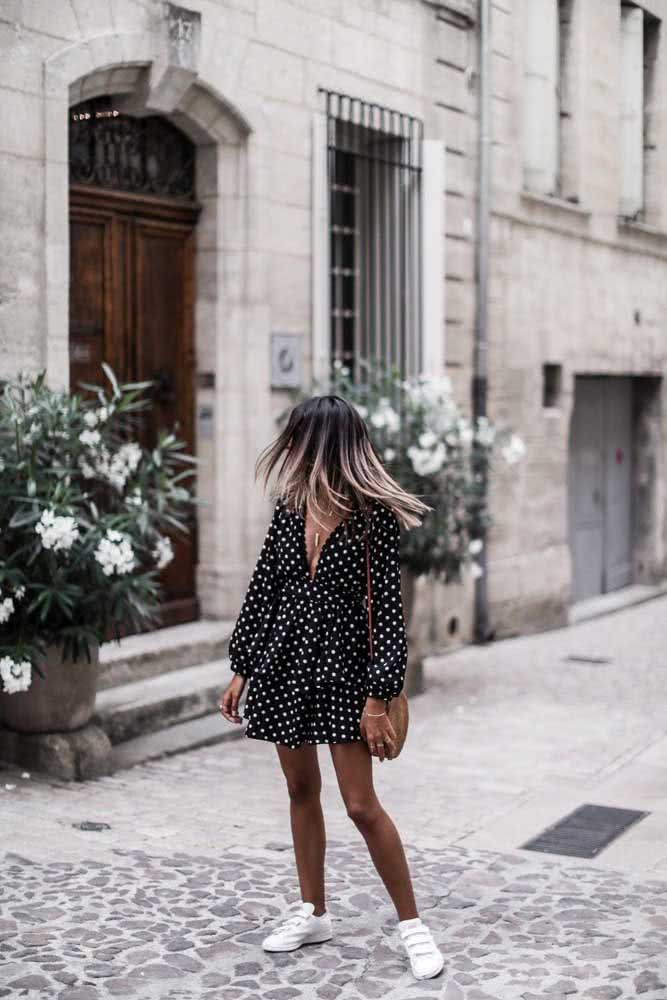 Um look com tênis branco básico e vestido curto preto de bolinhas cheio de leveza. 