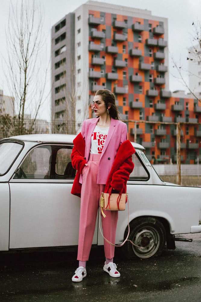 E por falar em looks ousados, dá uma olhada nesta ideia divertida e cheia de sofisticação com tailleur rosa, camiseta com estampa, casaco peludo vermelho e tênis casual branco. 