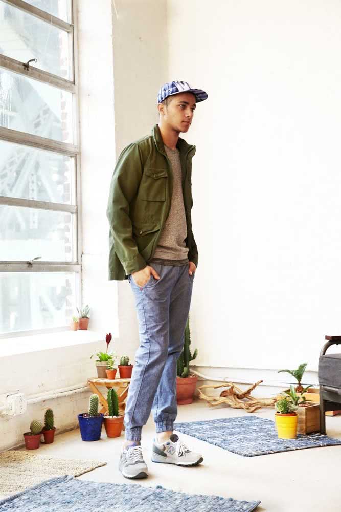 Dá uma olhada no estilo deste look com calça jogger jeans masculina, camiseta, jaqueta verde militar, tênis esportivo e boné. 