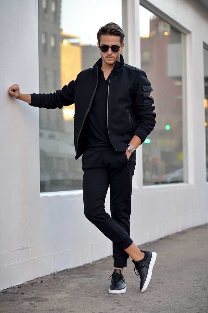 Um look all black cheio de sofisticação com calça jogger masculina preta de sarja, camisa, jaqueta parka e tênis casual de couro.
