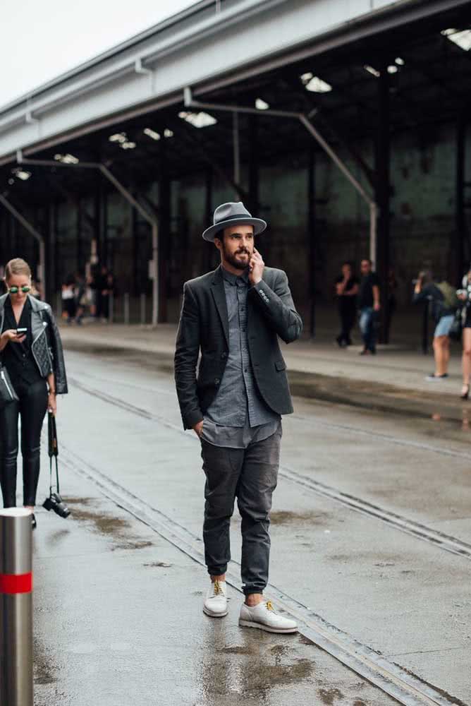 Um visual descontraído mas sem perder a elegância com calça jogger cinza, camisa, casaco de alfaiataria, chapéu e um oxford branco com cadarço cor de mostarda em contraste. 