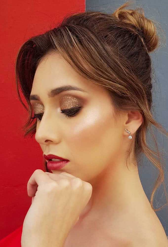 Olhos bem iluminados e marcantes com sombra dourada com glitter e batom vermelho nesta make poderosa para festa.