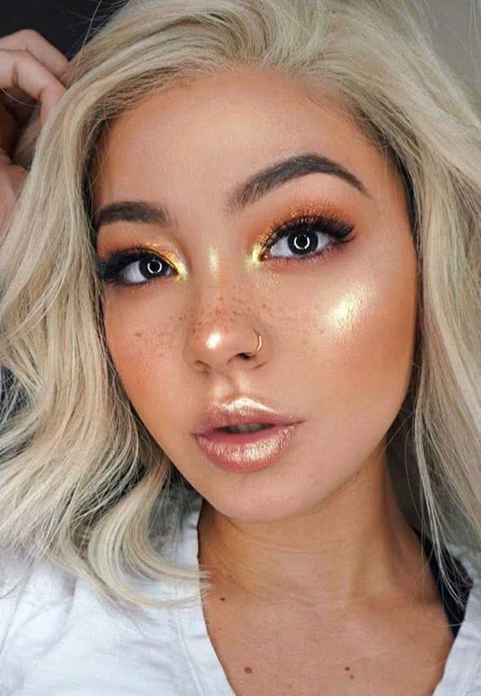 Uma make inspirada no brilho do pôr do sol com sombra laranja com um toque de dourado no canto interno do olho, além de um blush e batom também no mesmo tom e super iluminados.