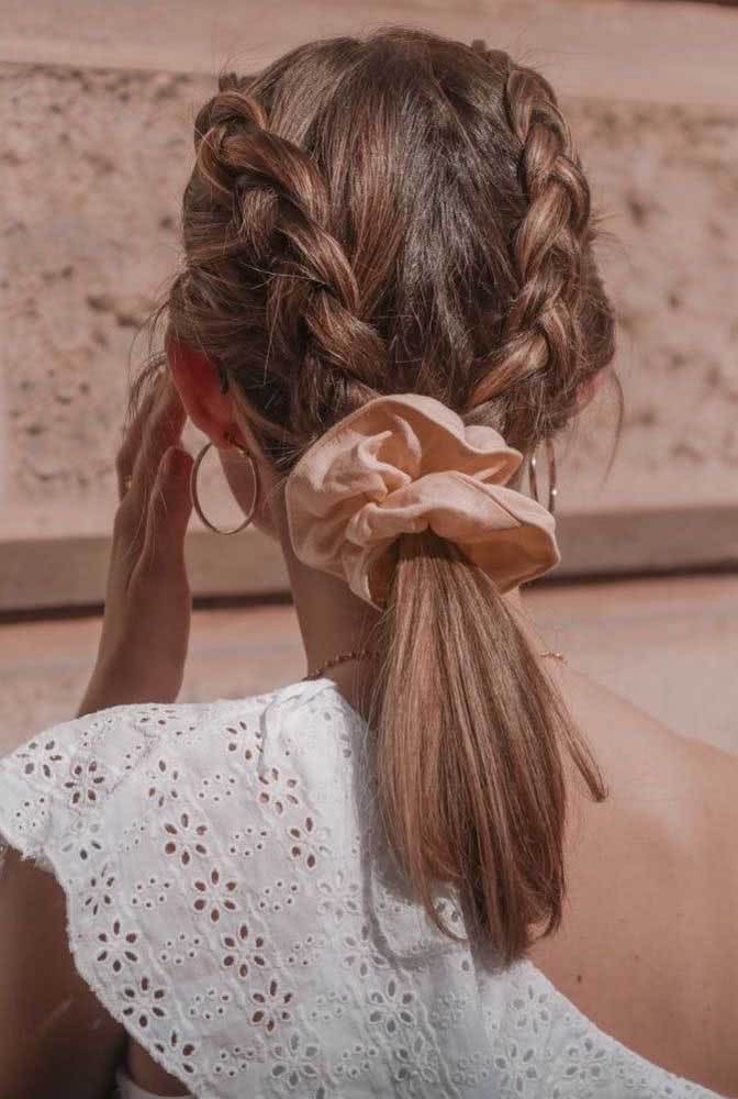 Um penteado fácil e super estiloso para cabelo médio, com duas tranças embutidas paralelas que se encontram em um rabo de cavalo baixo preso com um elástico estilo frufru. 