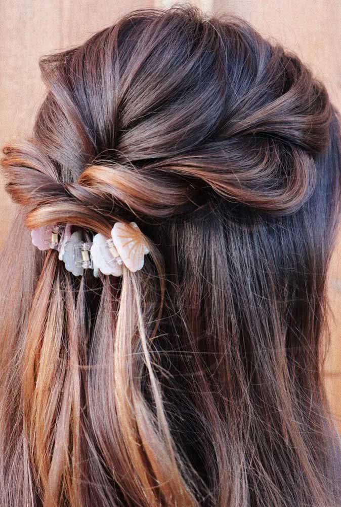 Penteado semi preso cheio de curvas com as mechas da parte da frente do cabelo se encontrando na parte de trás com uma torção soltinha e presilhas delicadas em formato de concha. 