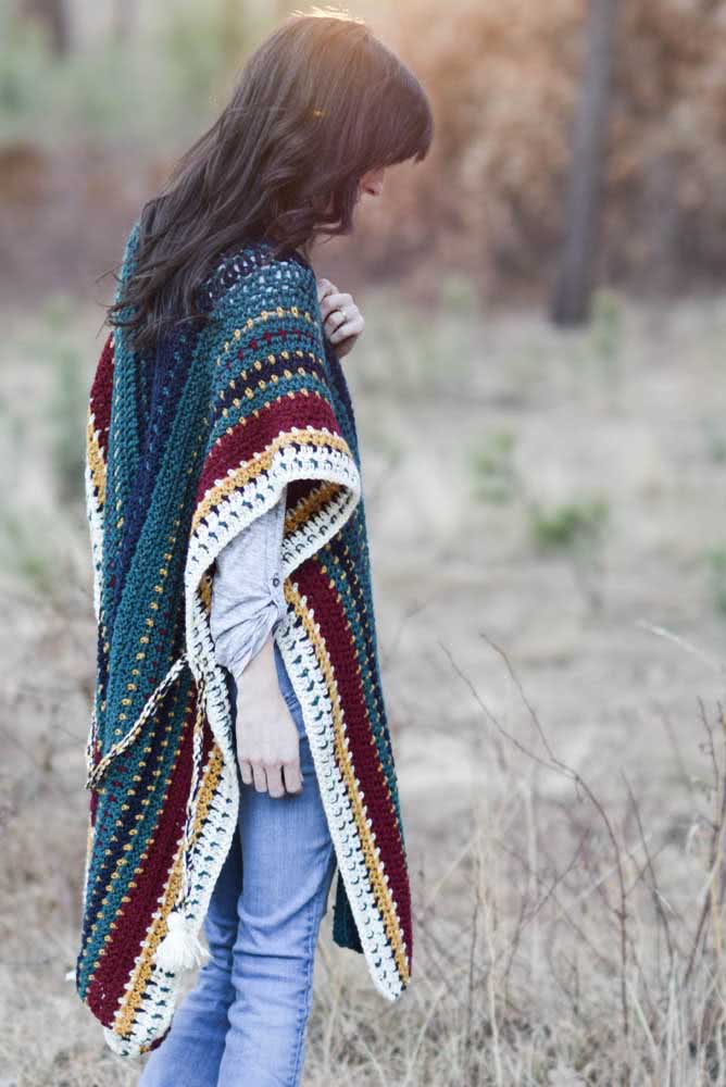 Poncho de crochê retangular verde com listras vermelhas, amarelas e brancas nas laterais para um look casual e descontraído para o outono-inverno.