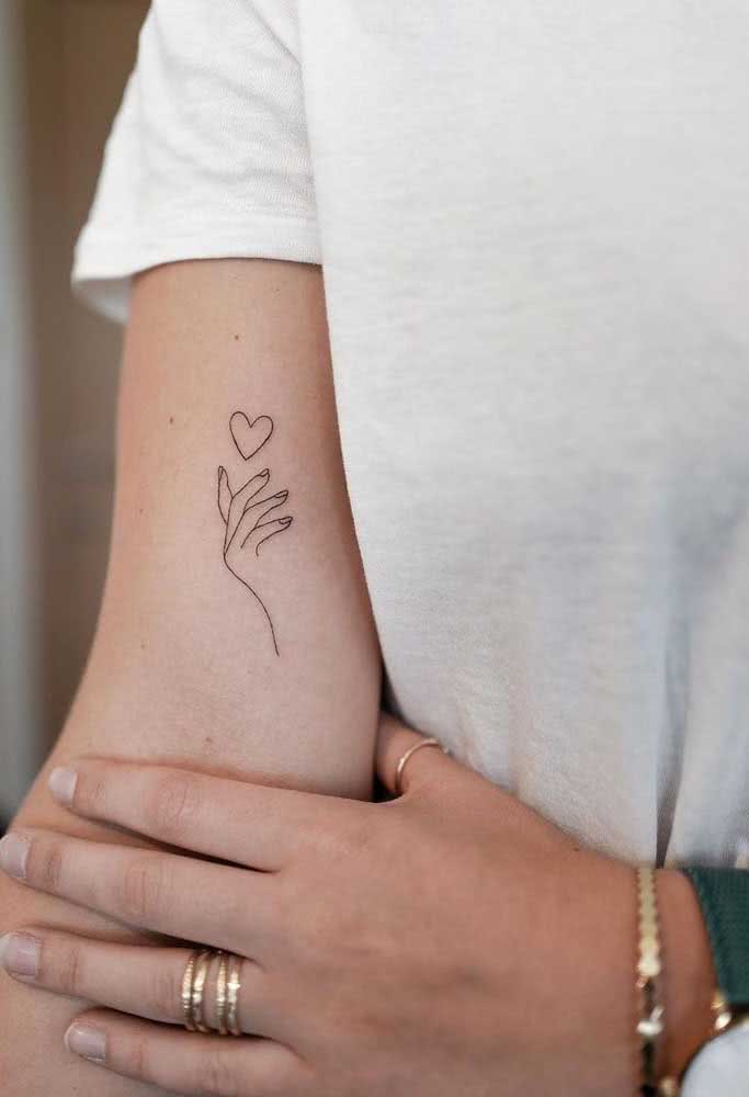 Para expressar amor e ternura, o desenho de uma mão invocando um coração nesta tatuagem minimalista feminina.