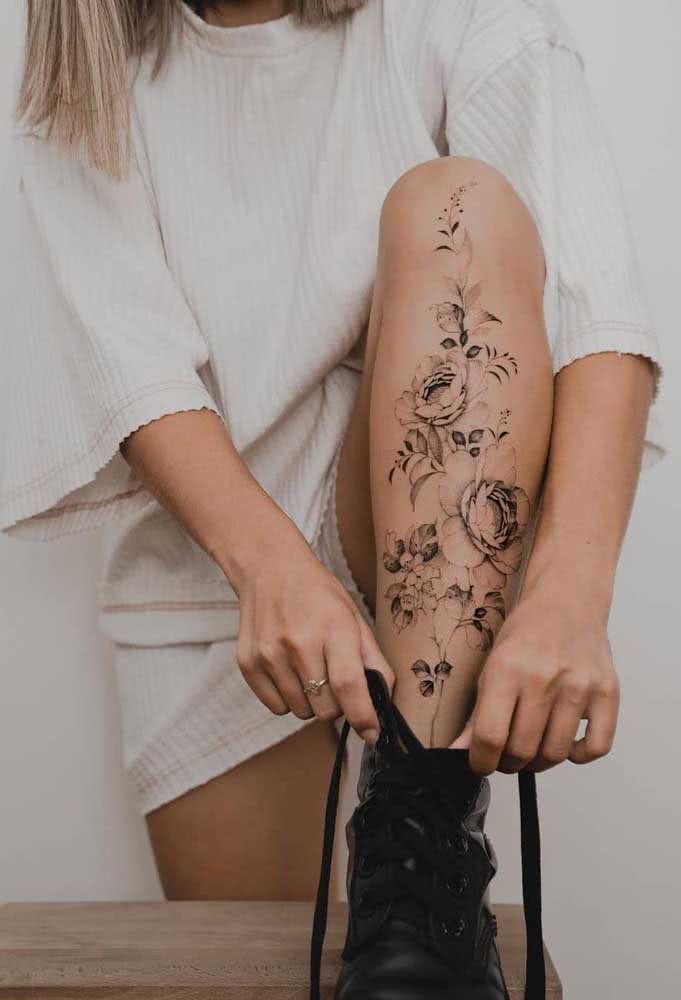 Um arranjo de flores com muitas folhas que se estende nesta tatuagem na perna feminina.