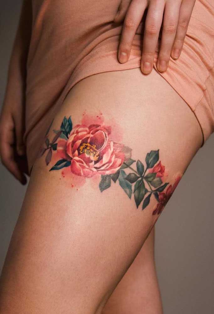 Mas se você quer fazer uma escolha mais ousada, confira esta tatuagem floral com cores vibrante e efeito aquarelado que forma uma cinta liga na coxa.