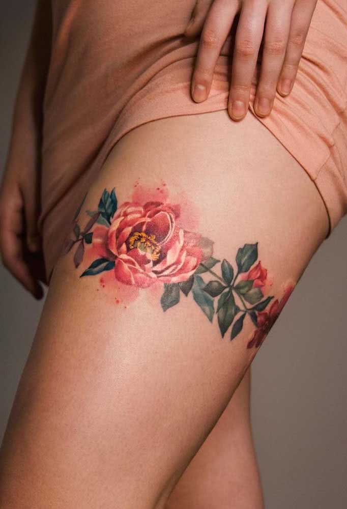 Mas se você quer fazer uma escolha mais ousada, confira esta tatuagem floral com cores vibrante e efeito aquarelado que forma uma cinta liga na coxa.