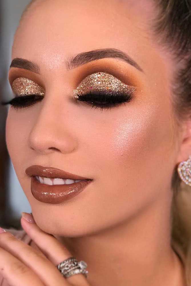 Um degradê marrom e laranja na pálpebra fixa demarcam bem o cut crease com glitter dourado nesta make poderosa, perfeita para festas à noite.