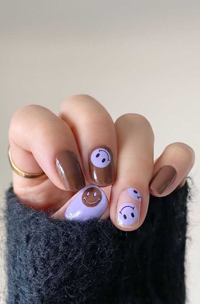 Smiley faces espalhadas pelas unhas decoradas em branco, bege e marrom. 