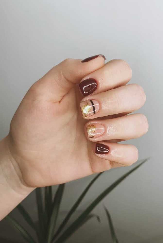 Já neste exemplo, as unhas gêmeas se destacam das demais bordô com uma faixa preta no centro e um toque de dourado sobre o tom natural da unha. 