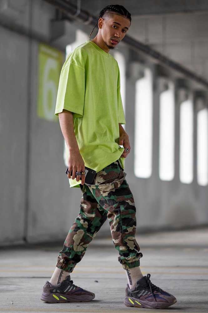 A camiseta larga verde limão faz o contraste perfeito com a calça camuflada jogger masculina, num look de destaque.