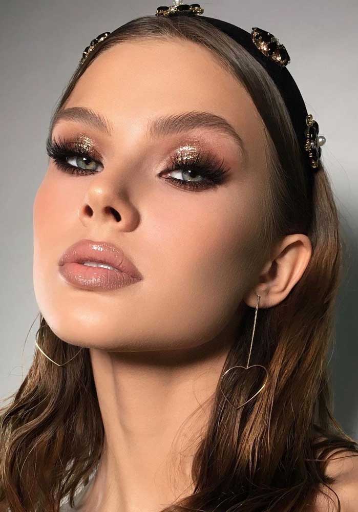 Um olhar marcante com cílios alongados, sombra marrom esfumada com um o que de glitter dourado e batom nude gloss com contorno.