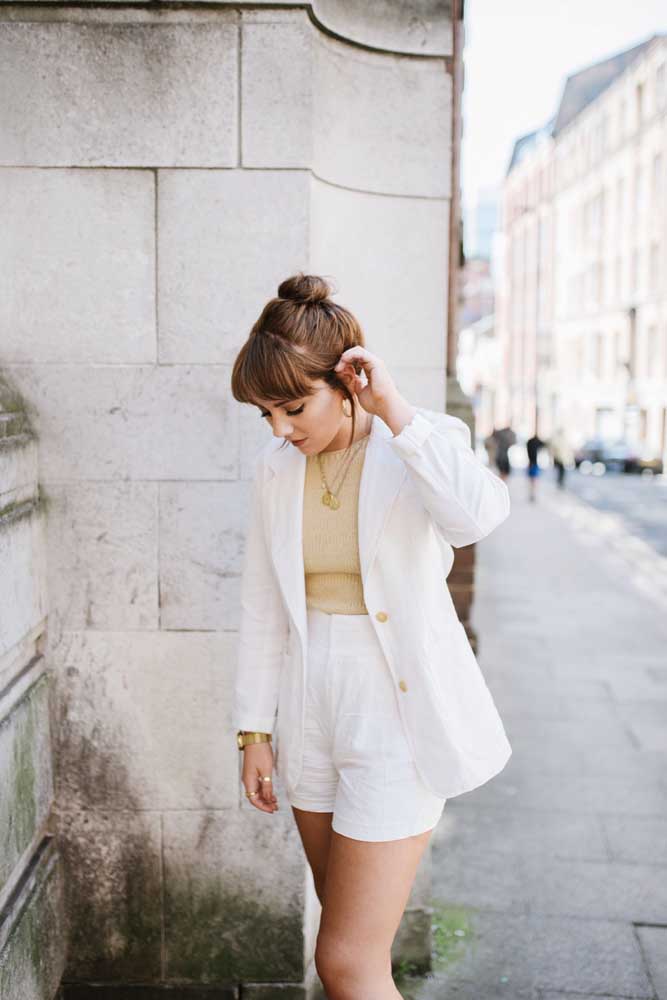 Short social e blazer brancos combinados com blusa de tricô num tom claro de dourado.