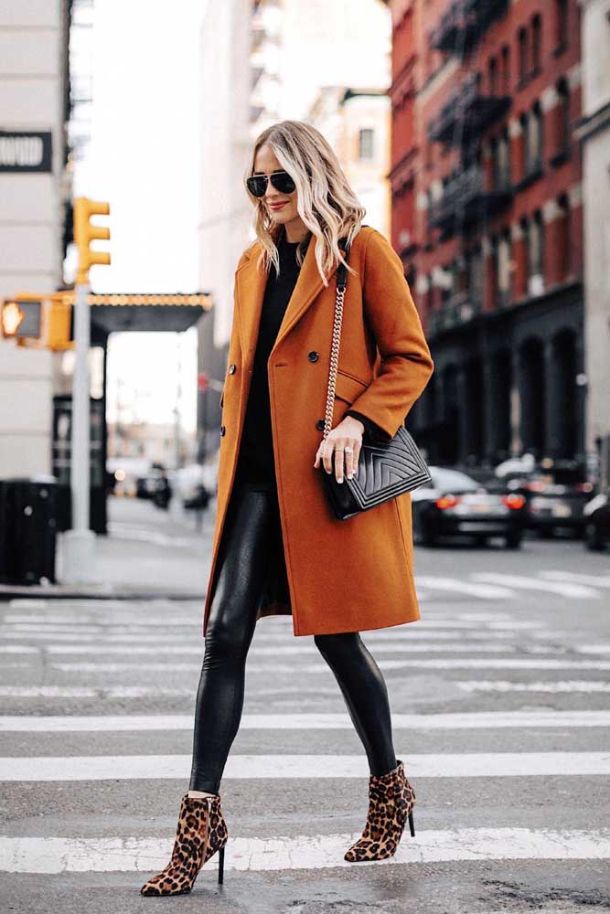 Um look com calça legging de inverno digno de uma fashionista, com casaco longo laranja e bota de salto alto fino e cano baixo com estampa de oncinha.