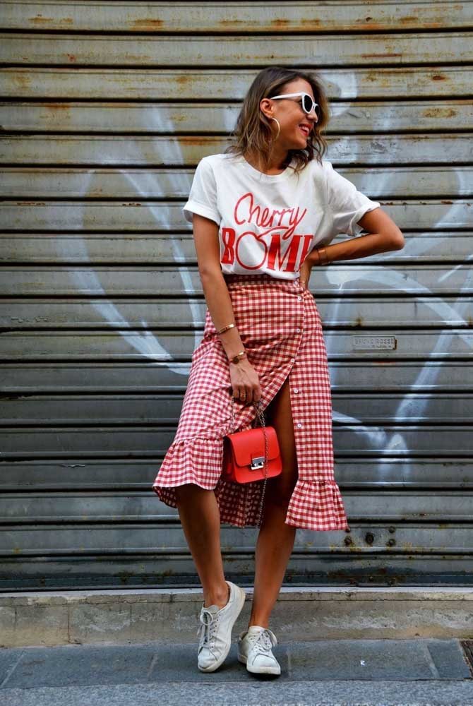 Despojado e cheio de atitude, um visual com camisa branca estampada com saia midi xadrez com botões abertos formando uma fenda e tênis branco básico. 