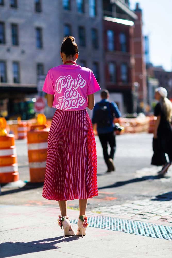 Digno de uma fashionista, um look divertido e super moderno com camiseta pink estampada, saia midi plissada da mesma cor e salto alto decorado com flores.