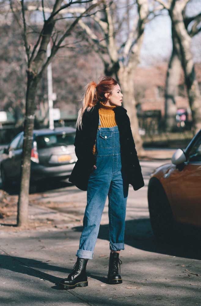 Um look bem quentinho e estiloso com macacão jeans, suéter de lã com gola alta, casaco e coturno preto.