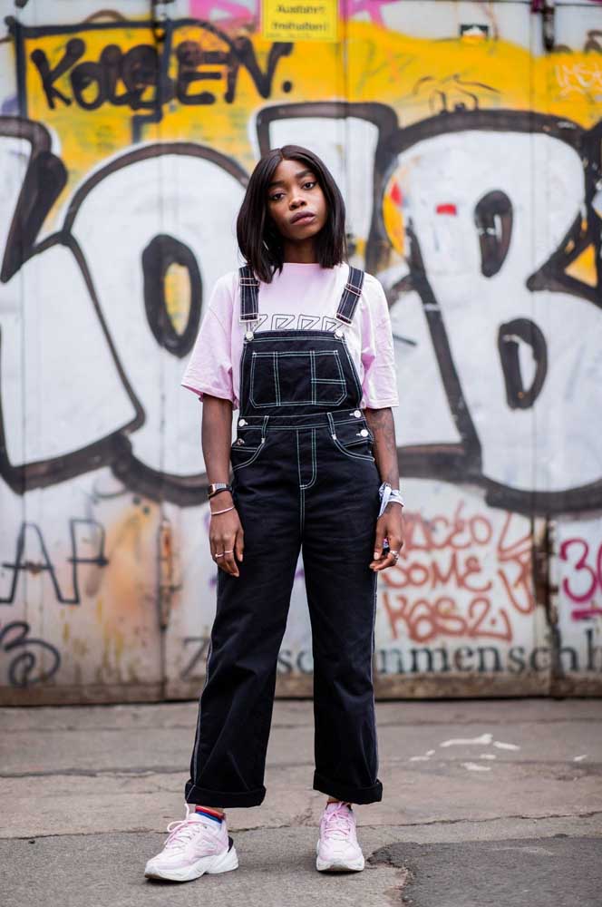 Macacão jeans preto com costura branca, camiseta e sneakers: inspiração direta da moda urbana dos anos 1990 que está com tudo atualmente!