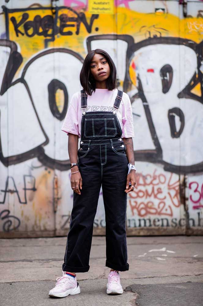Macacão jeans preto com costura branca, camiseta e sneakers: inspiração direta da moda urbana dos anos 1990 que está com tudo atualmente!