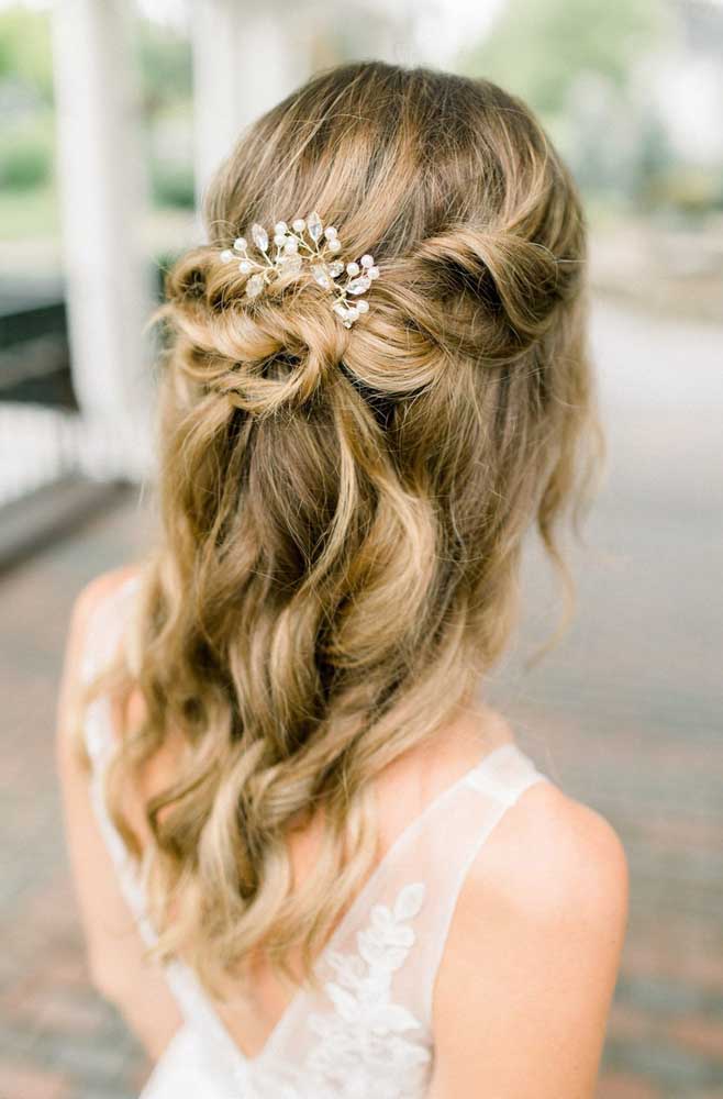 As mechas da frente se encontram numa trança adornada com uma presilha floral neste penteado para casamento, com o restante do cabelo solto. 