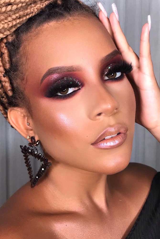 Dá uma olhada nessa ideia de maquiagem para pele morena com degradê de bordô para preto com bastante glitter na sombra, combinando com blush e batom acobreados. 