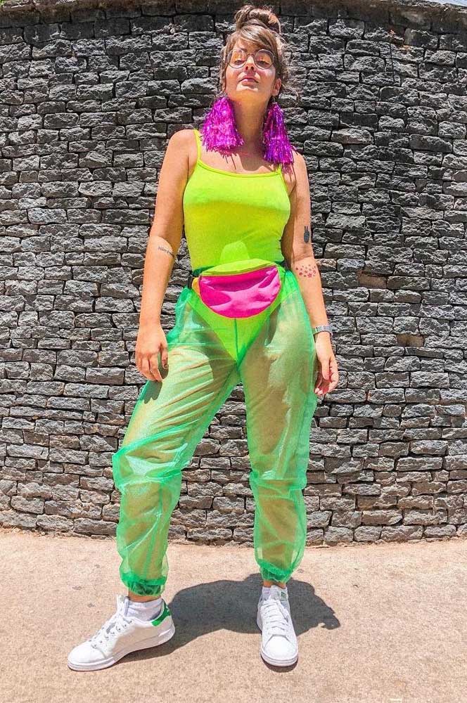 Alegria, diversão e muita atitude: são essas as palavras que definem esse look com roupas anos 80 para festa, com body verde neon, calça jogger verde transparente, pochete rosa, tênis branco e brincos pompom metalizado.