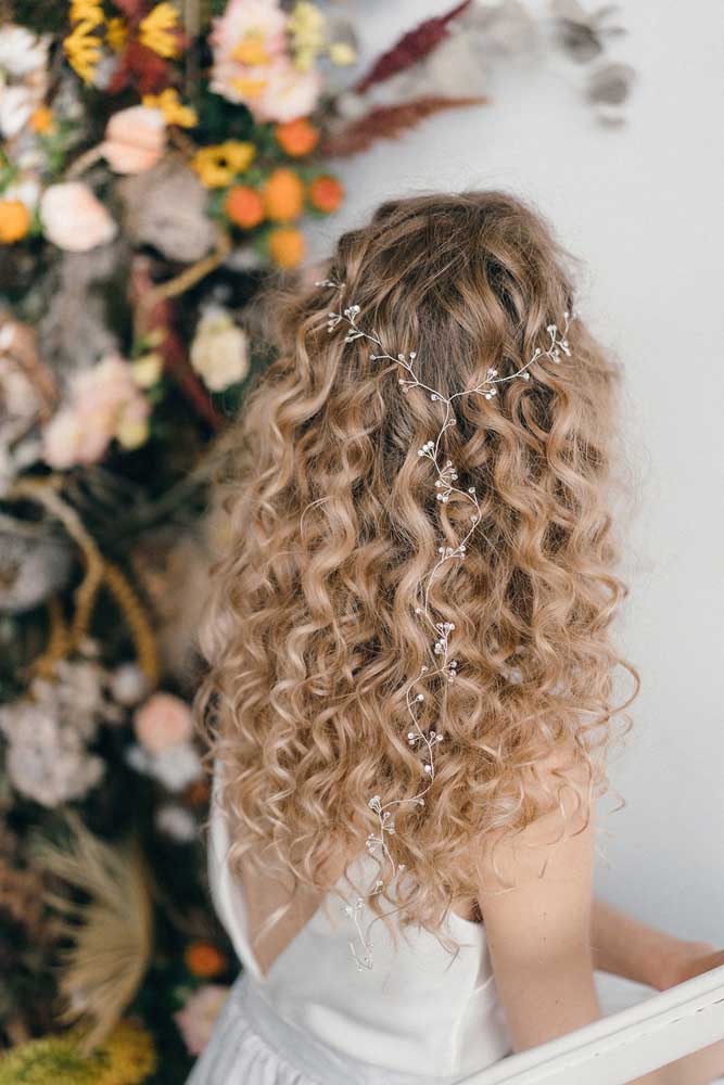 Simplicidade e muita delicadeza nesse penteado para cabelo cacheado solto com uma coroa prateada floral. 