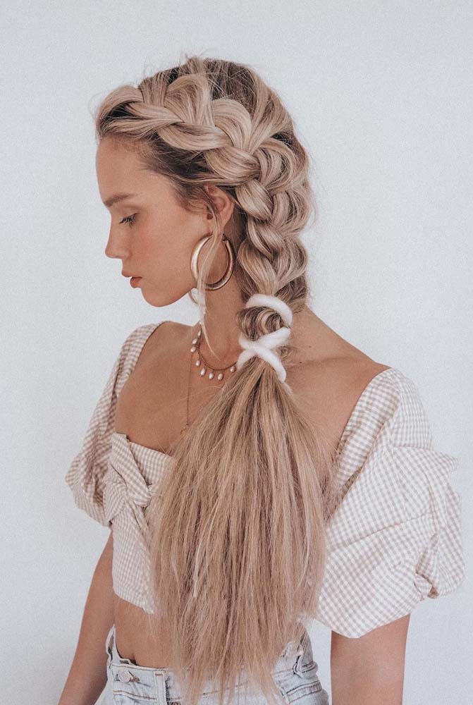 Penteado com o cabelo preso fácil, jovial e charmoso: jogue todos os fios para um lado e comece uma trança embutida lateral soltinha, quando ela chegar na altura do ombro, prenda e penteie as pontas para deixá-las bem volumosas.