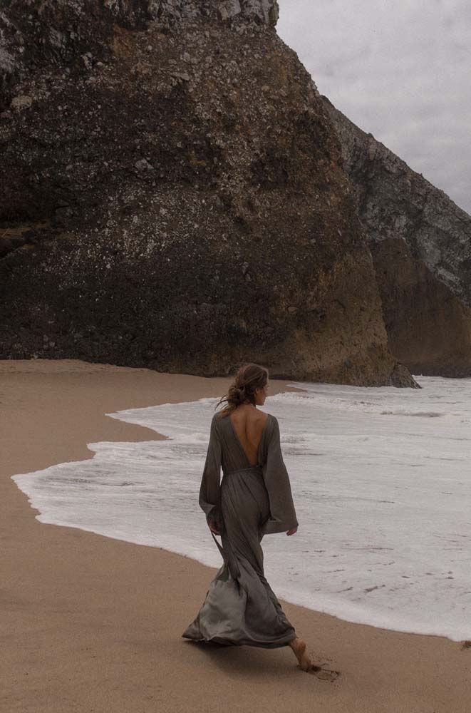Uma caminhada cheia de dramaticidade na praia que une a monumentalidade da pedra, o momento da onda e a leveza do vestido.