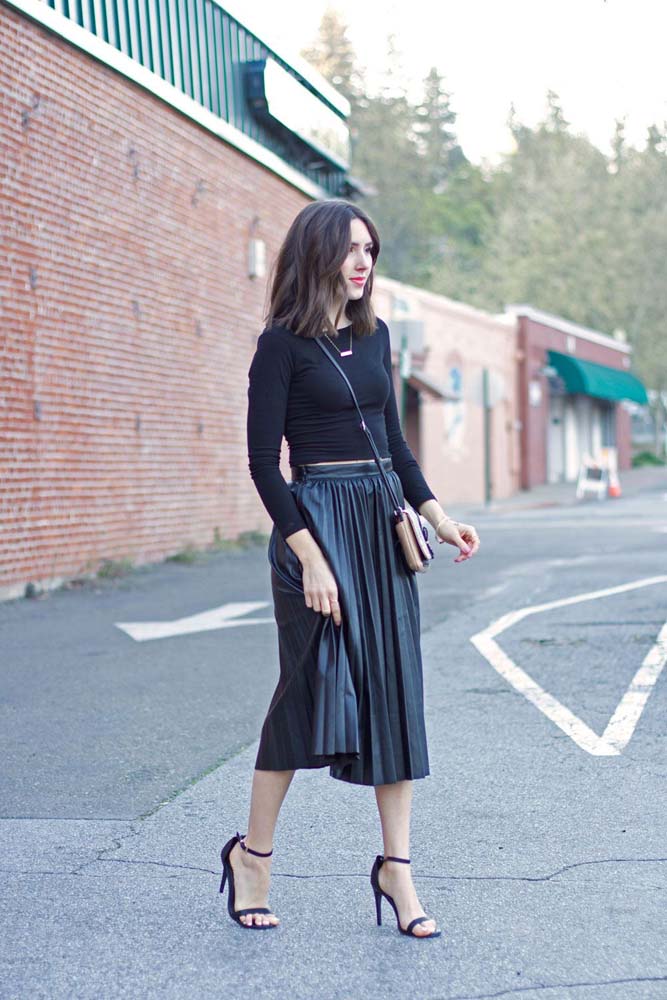 Um look para festa all black com saia preta plissada em tamanho midi, com blusa de manga longa e sandália de tiras.