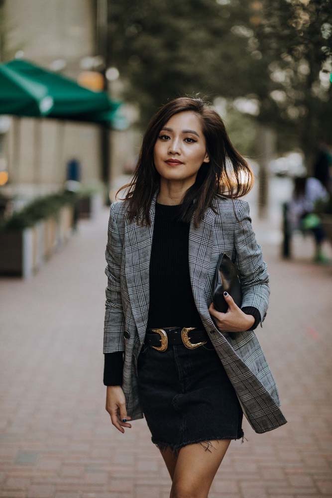 Look despojado com saia preta jeans, blusa de manga longa na mesma cor e blazer xadrez cinza. 