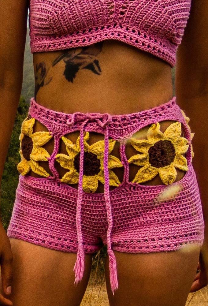Nesse modelo aqui, o destaque são os girassóis que formam um tipo de cinturão vazado no shorts de crochê rosa. 