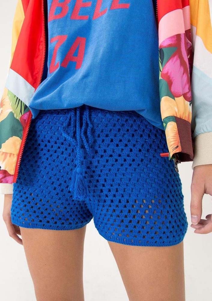 Shorts de crochê azul anil, camiseta e jaqueta leve e colorida: um exemplo de como incorporar essa peça também nos seus looks urbanos.