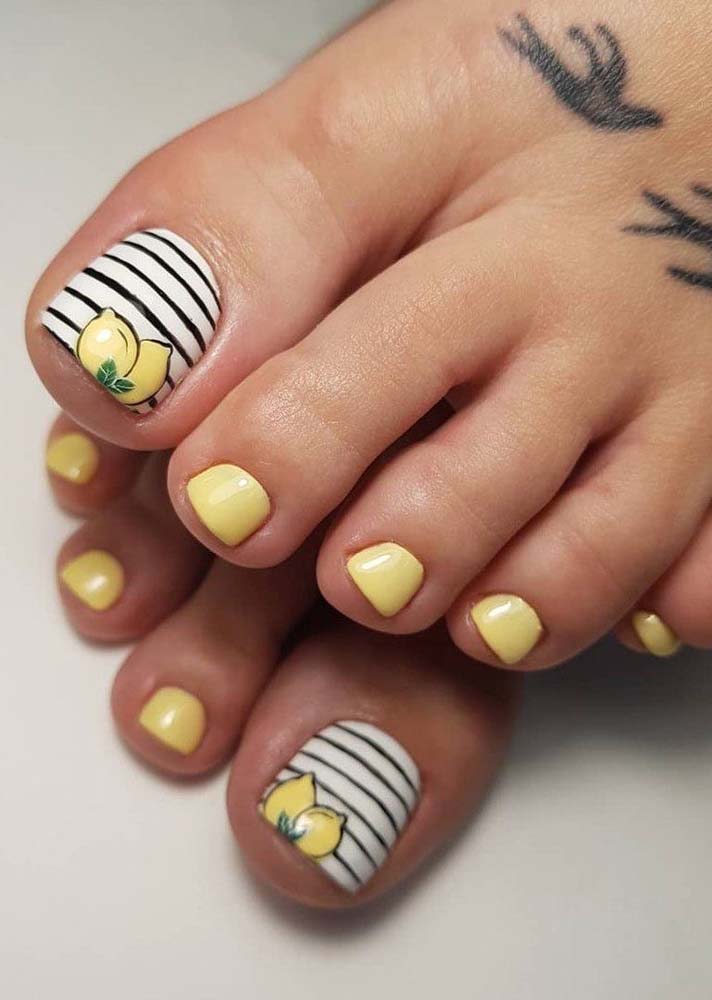 Amarelo pastel nos limões sicilianos desenhados no dedão com fundo listrado P&B e nas demais unhas, fazendo uma cobertura lisa. 