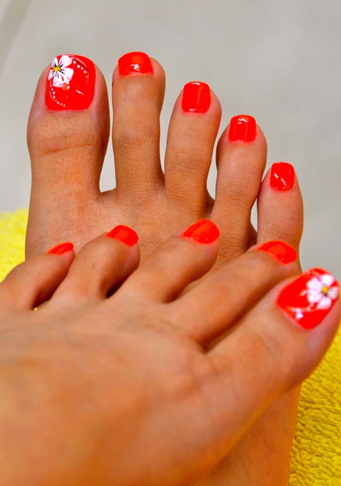 Mas se você quer ousar, aposte em unhas do pé vermelhas decoradas com uma flor branca.