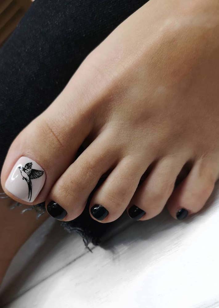 No dedão, o fundo branco tem aplicação de adesivo de um pássaro desenhado e as demais unhas esmaltadas totalmente em preto. 
