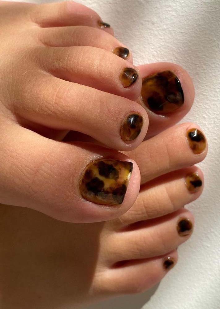 Unhas do pé decoradas em dourado com alguns toque de preto e marrom num visual marmorizado, como de uma pedra preciosa.