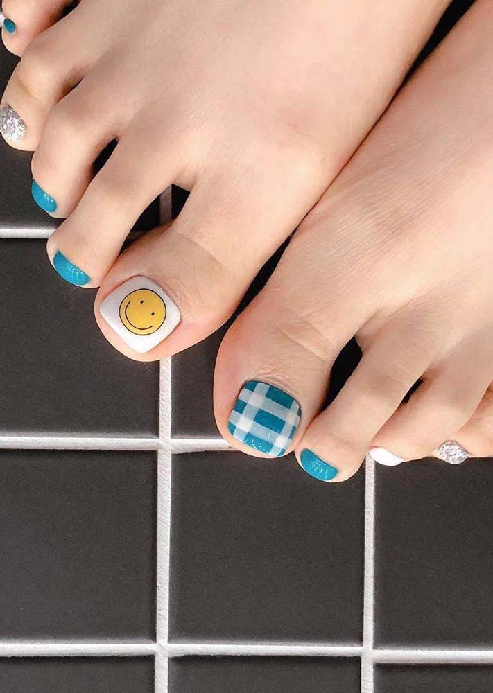 Enquanto as unhas menorzinhas são cobertas totalmente por esmaltes coloridos e com glitter, as unhas do dedão do pé tem mais espaço para uma smiley face e um padrão xadrez.