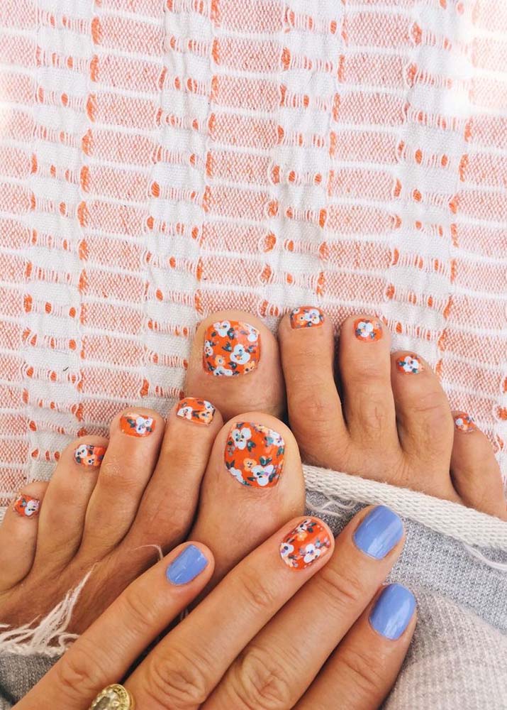 Tudo combinando: unhas do pé decoradas com padrão florido em fundo laranja, que aparece também na filha única da unha da mão. 