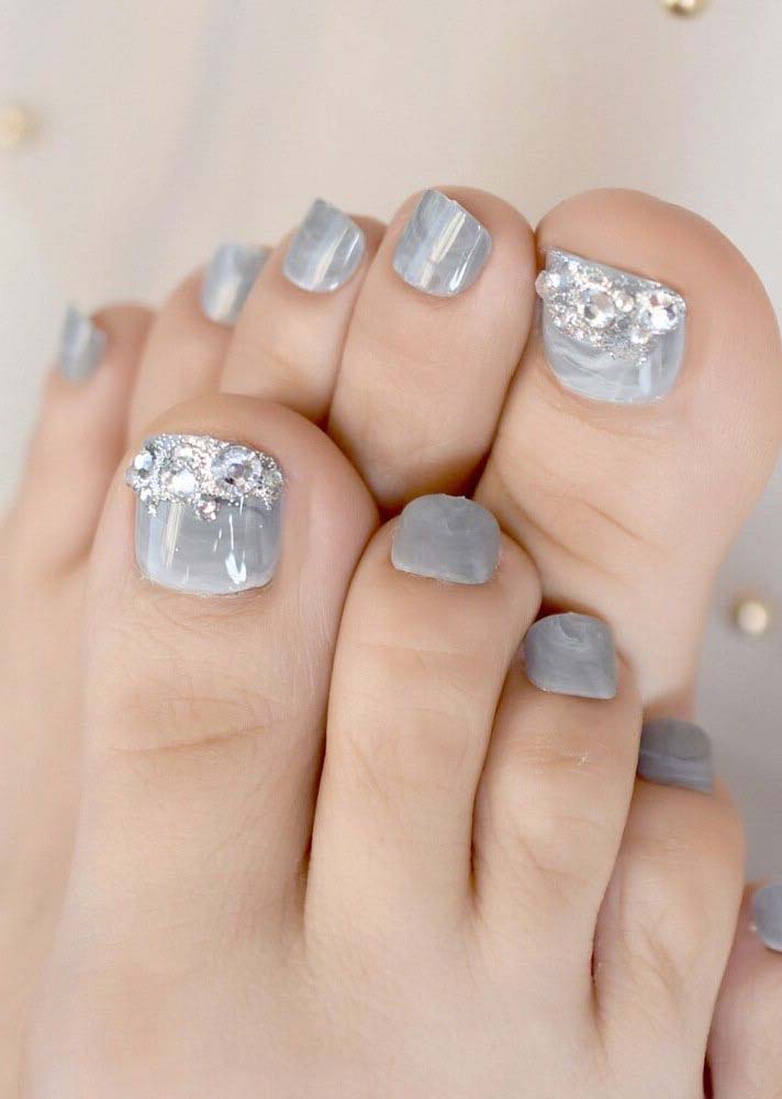 Muita delicadeza nessas unhas do pé decoradas com pedrinhas transparentes sobre o esmalte cinza claro. 